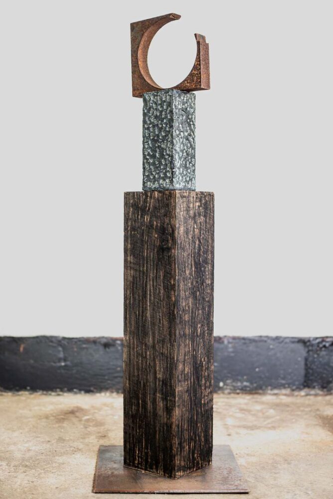 Skulptur ‚Hohes C' (2026) von Manfred Egersdoerfer: ein rostiges Stahlelement in offener C-Form auf einem genarbten Steinblock und einem dunklen Holzsockel.
